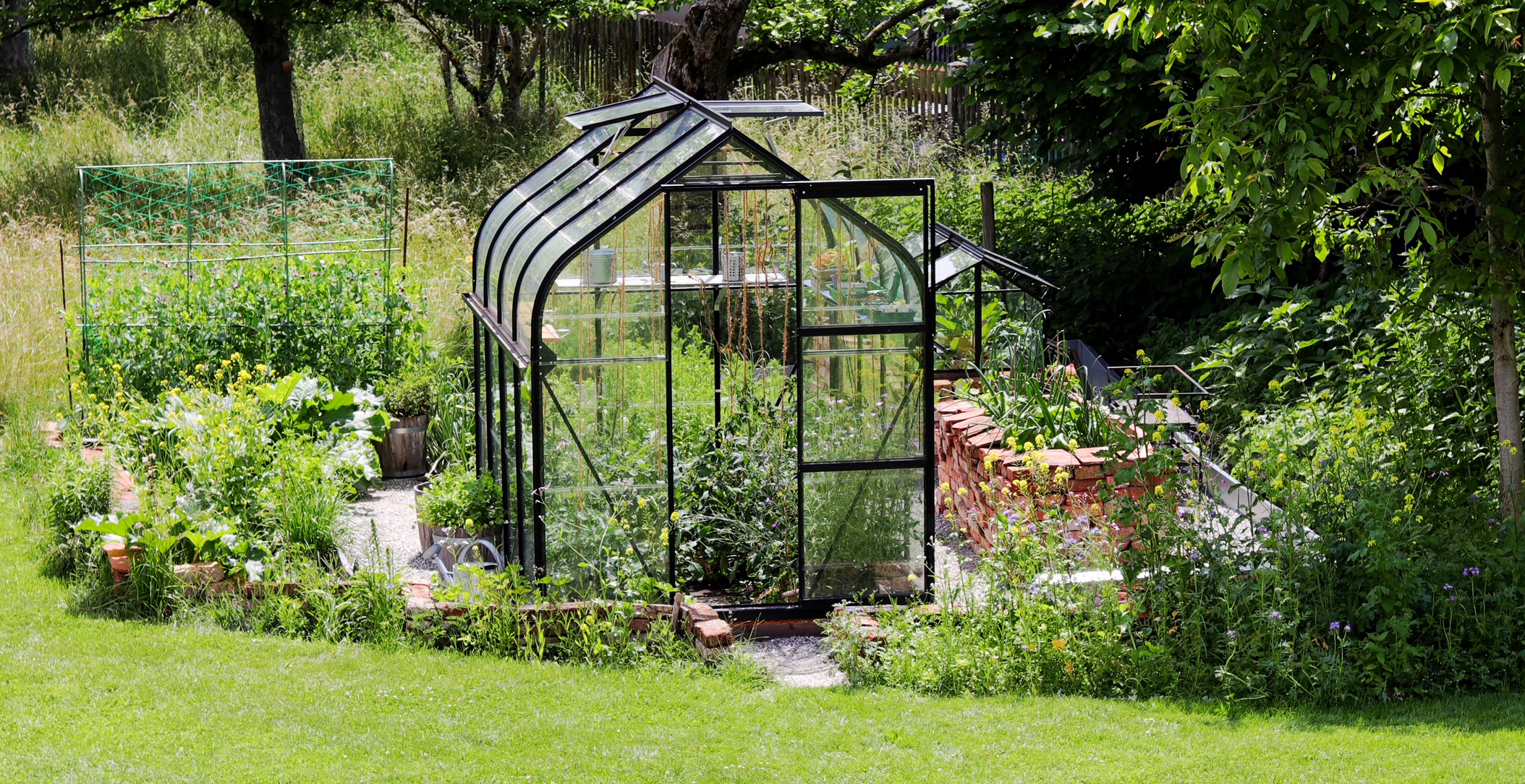 Vitavia Gewächshaus Orion in einem üppig grünem Garten im Sonnenlicht